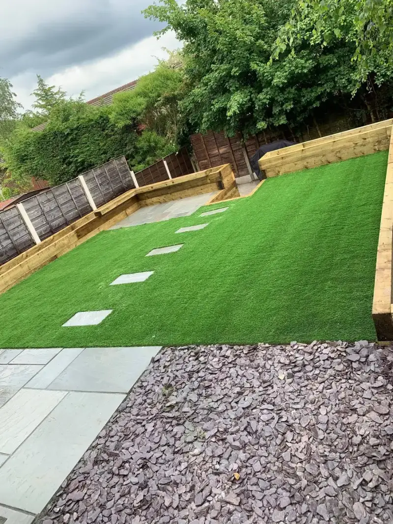 Artificial lawn with grey stepping stones, sleeper raised beds and slate chippings