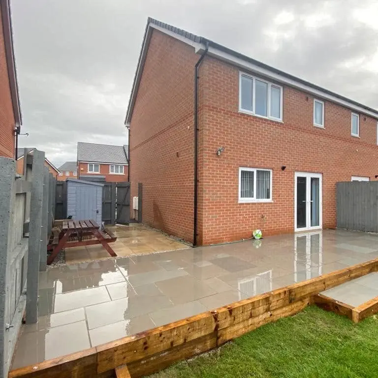 After: raised porcelain patio with an oak sleeper edge and a step down to the lawn behind a new-build semi