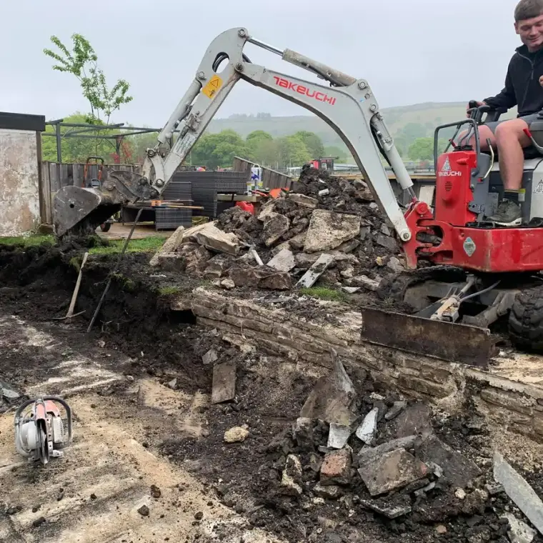 Mini digger breaking out an old stone garden wall ready for new footings