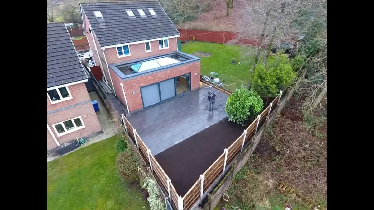 Drone view of a finished patio and fencing behind a detached house with a roof lantern extension