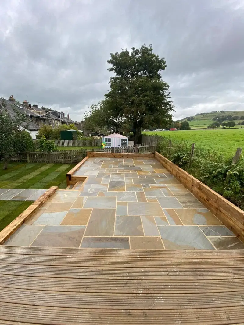 Indian sandstone patio with sleeper edging and timber decking, backing onto fields