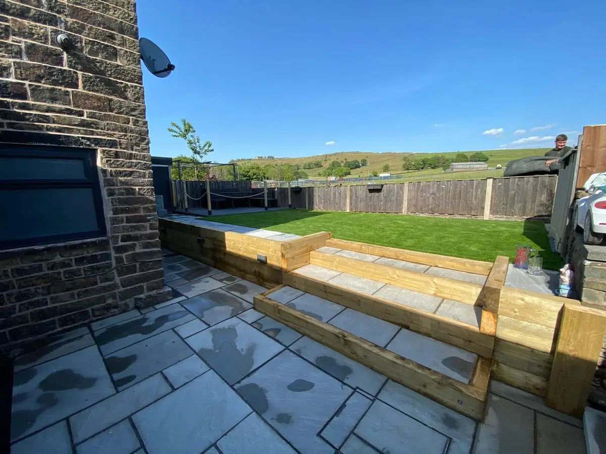 Grey patio with oak sleeper steps up to a lawn, with moorland behind